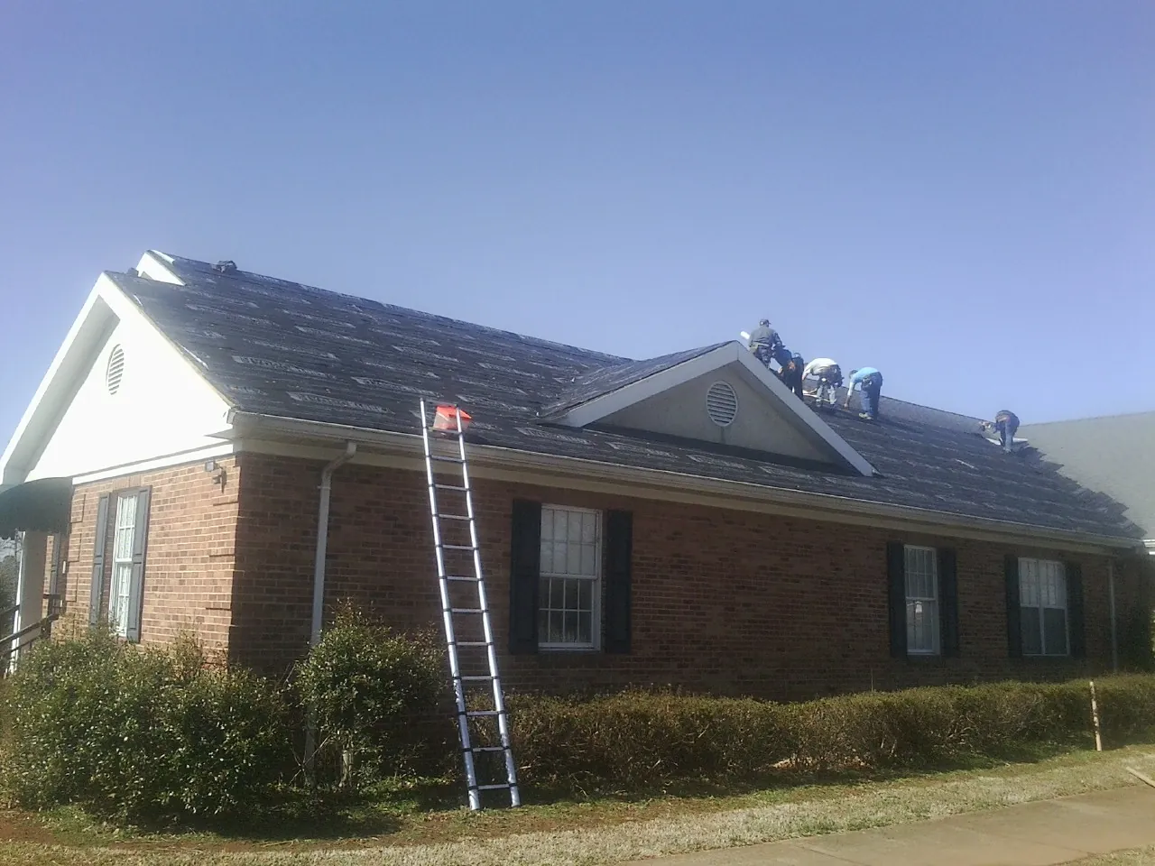 Crew tearing shingles off a brick ranch roof with a ladder set — Emergency Roof Repair work by our crew in Lincolnton