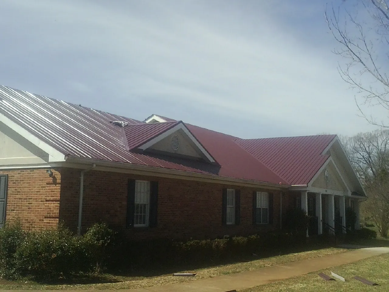 Red metal roof with gabled entries on a long brick building, from a Hail Damage Roof Repair job in Lincolnton