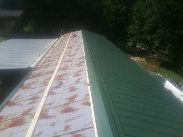 Old rusted panels beside newly installed green metal roofing — Wind Damage Roof Repair by Roofing Brothers in Lincolnton