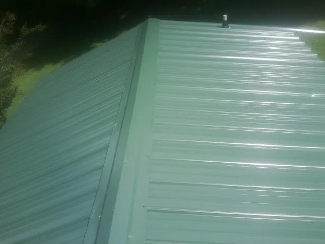 New green metal panels meeting at the ridge of a roof — Flat Roof Repair work by our crew in Lincolnton