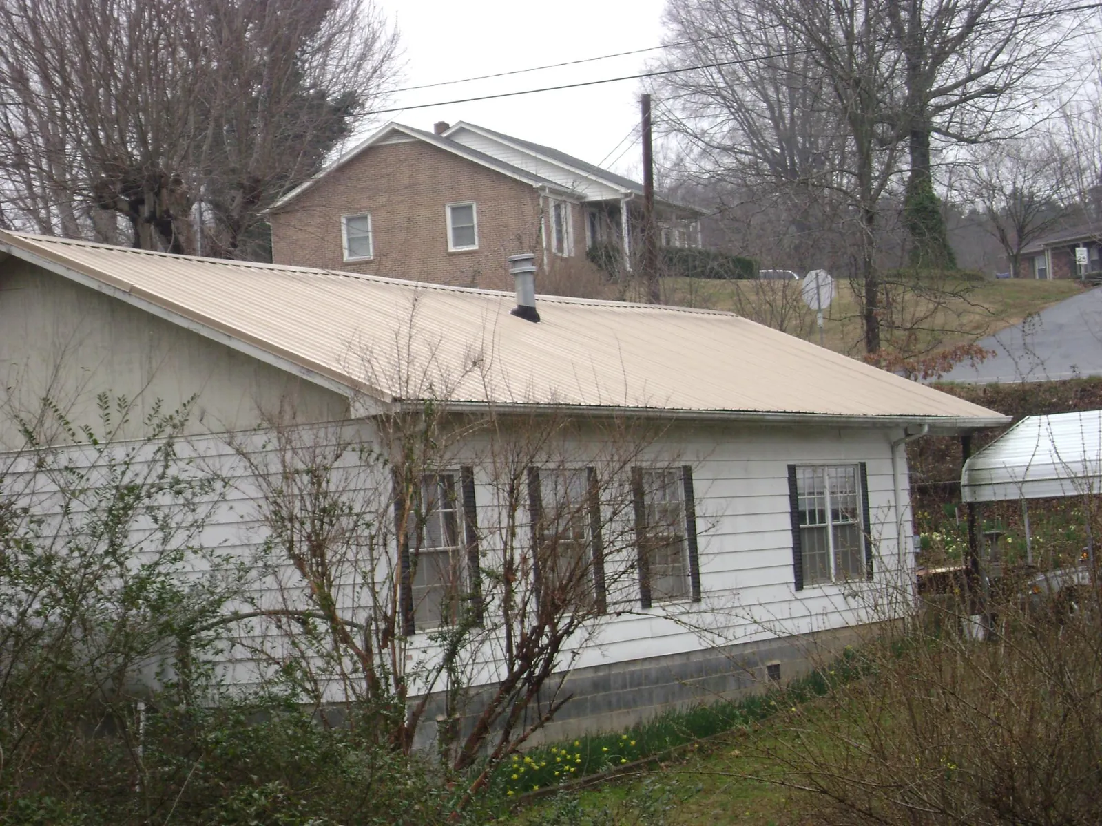 Tan metal roof on a white sided house set into a hillside — Commercial Roofing by Roofing Brothers in Lincolnton